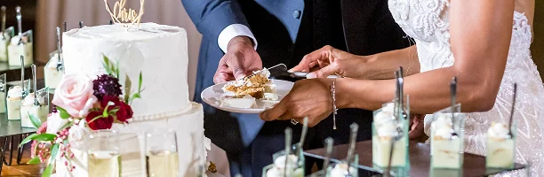 Bruid en bruidegom die samen hun bruidstaart snijden tijdens de receptie, omringd door drankjes en bloemdecoraties.