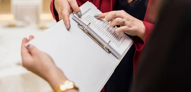 Evenementplanner die een afgedrukte checklist voor de bruiloftsvoorbereiding met een klant bekijkt tijdens een coördinatievergadering.