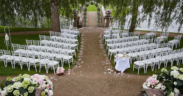 Buiten bruiloft ceremonie zitplaatsarrangement met witte stoelen, bloemdecoraties en een gangpad voorbereid voor gasten.