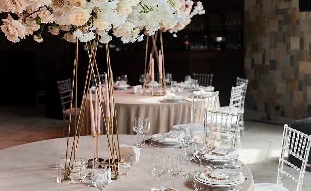 Bruiloftsbancetzaal met ronde tafels, hoge bloemstukken en elegante tafelsettings voor receptiegasten.